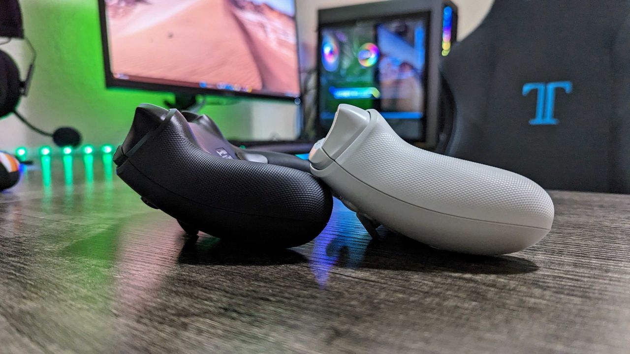 Two sleek gaming controllers, one black and one white, rest on a dark wooden desk in a modern gaming setup. A glowing monitor and gaming chair are in the background.