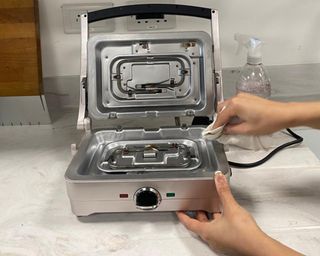 Christina Chrysostomou cleaning waffle maker with anti-bacterial spray and paper towel