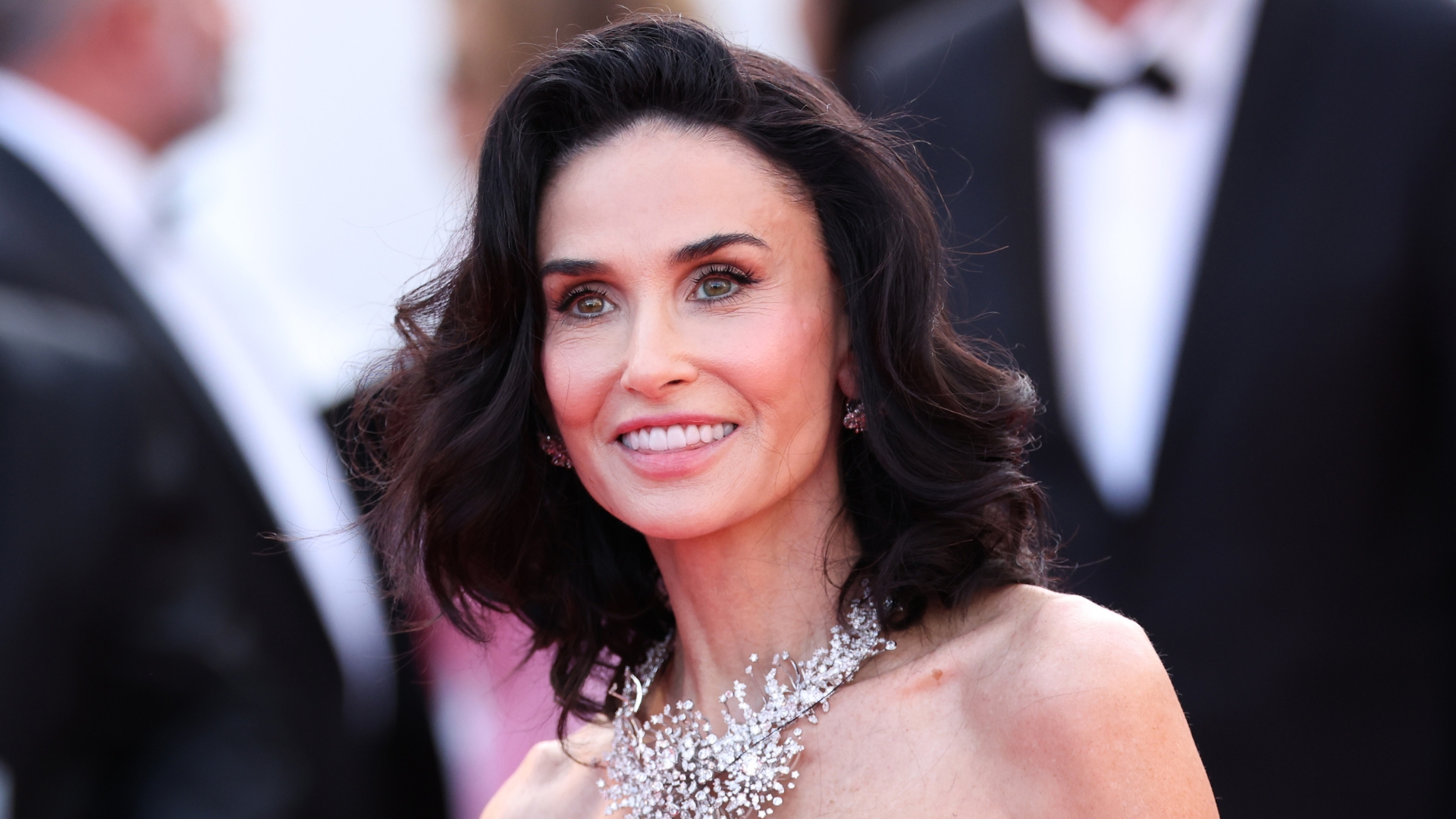 Image of Demi Moore smiling with curly brunette bob, wearing strapless dress and diamond necklace