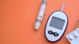 A grey and blue blood sugar monitor photographed on an orange background
