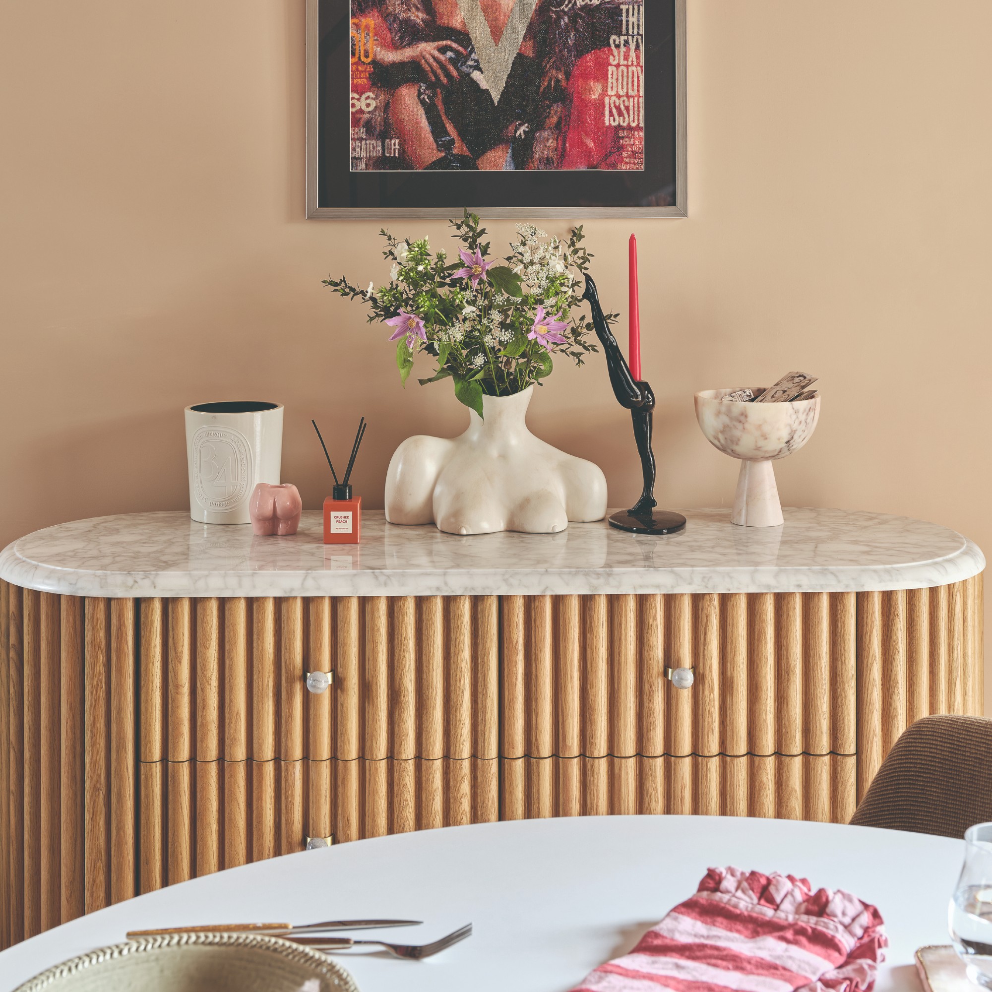 A pink-painted dining room with a reeded marble-top sideboard displaying a quirky flower vase and a candle holder by Anissa Kermiche