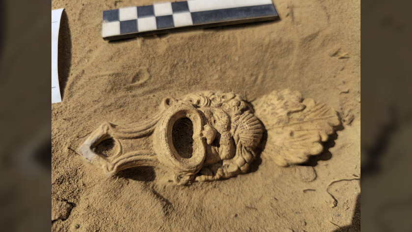 a clay-colored Roman oil lamp in the shape of a comic mask in the dirt