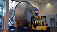 a forklift carries a large silver cylindrical through a doorway