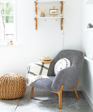 A white nursery corner with gray upholstered armchair and woven foot rest.