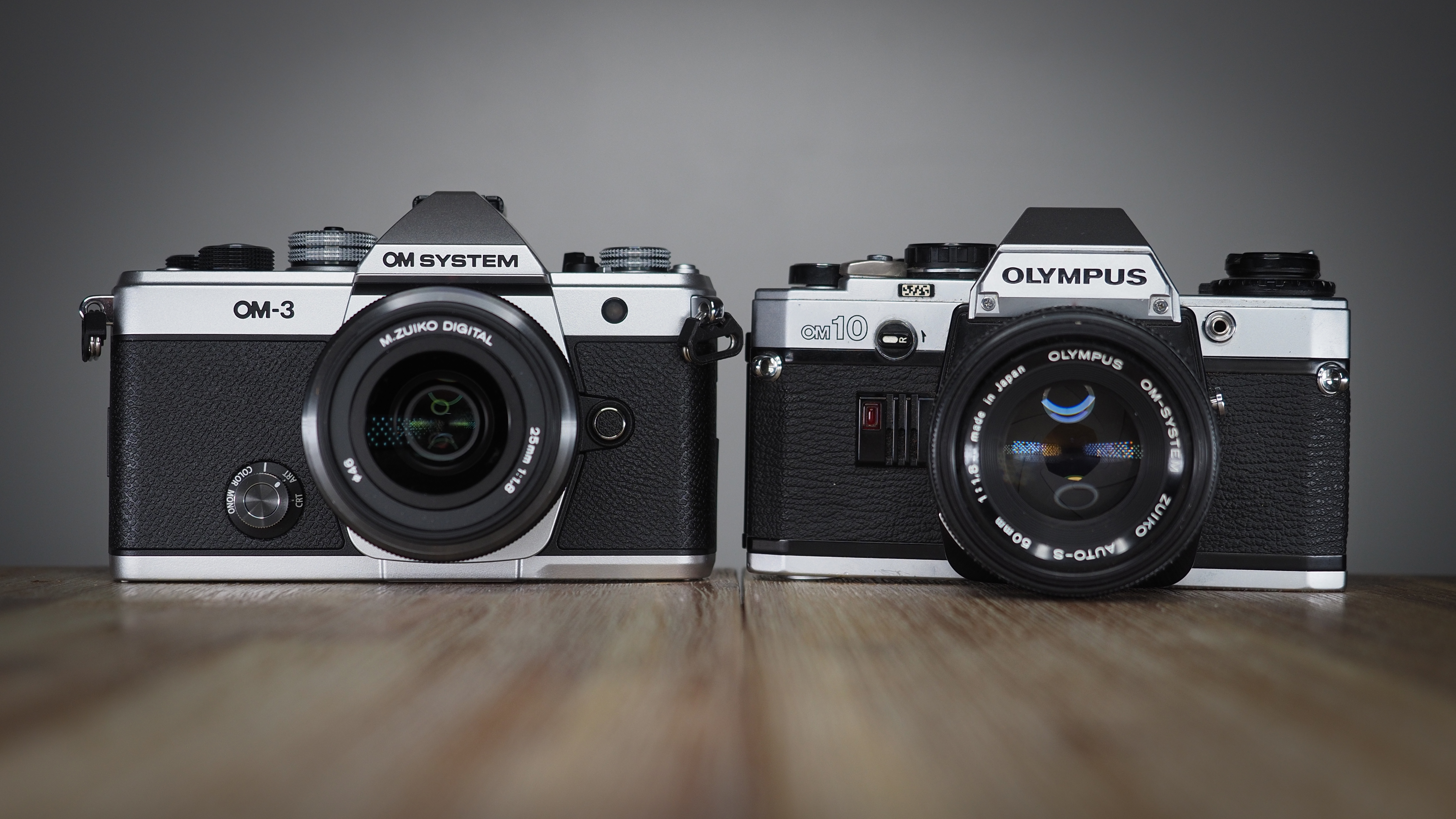 OM System OM-3, next to an Olympus OM-10, on a wooden surface