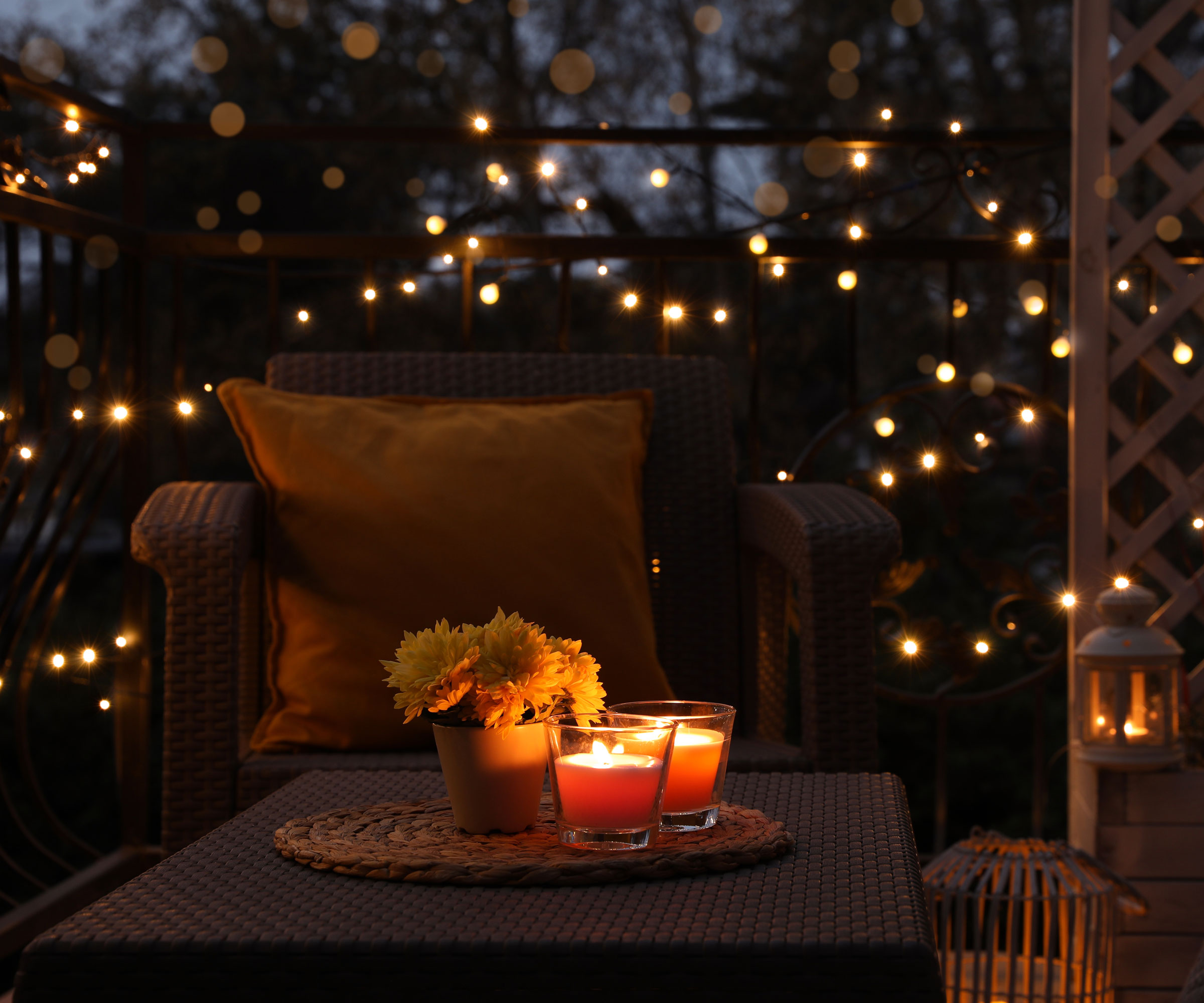 garden patio at night with string lights, trellis, garden chair and table, and some candles
