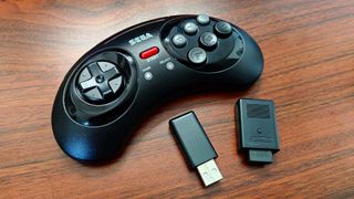 Retro-bit wireless Sega Genesis controller next to two dongles on woodgrain desk