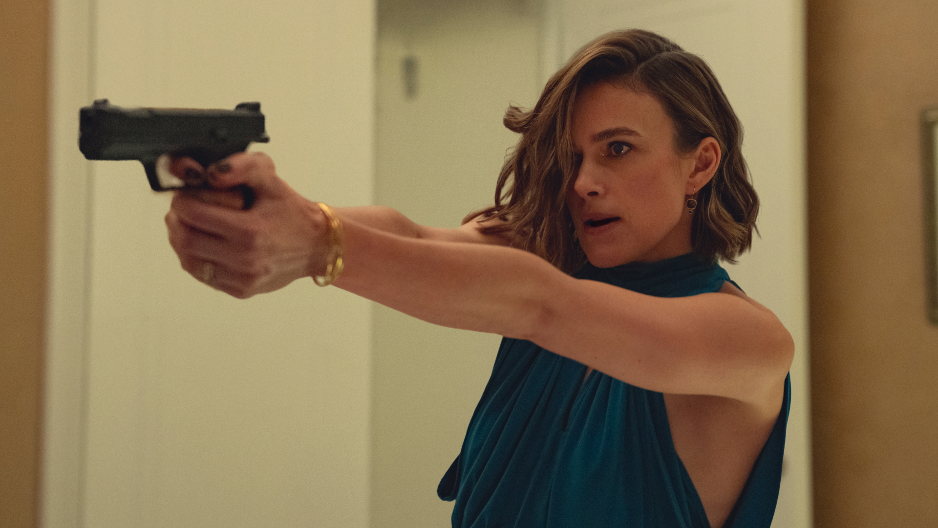 keira knightley wears a blue halter dress and points a gun in a still from black doves season 2
