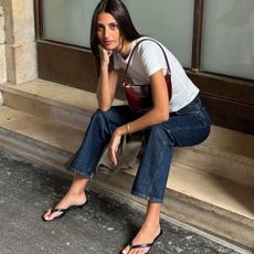 A French woman wearing a white tee, jeans, and flip-flop kitten heels