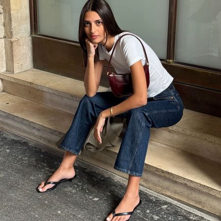 A French woman wearing a white tee, jeans, and flip-flop kitten heels