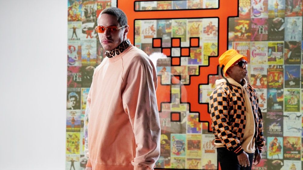 Pete Davidson and Chris Redd posing in front of a wall of movie posters in SNL skit