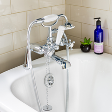 Roll top bath with a silver mixer tap with a shower attachment beside a white tiled wall.