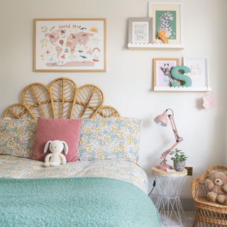 kids bedroom with woven headboard and floral bedlinen with gallery wall and pink lamp