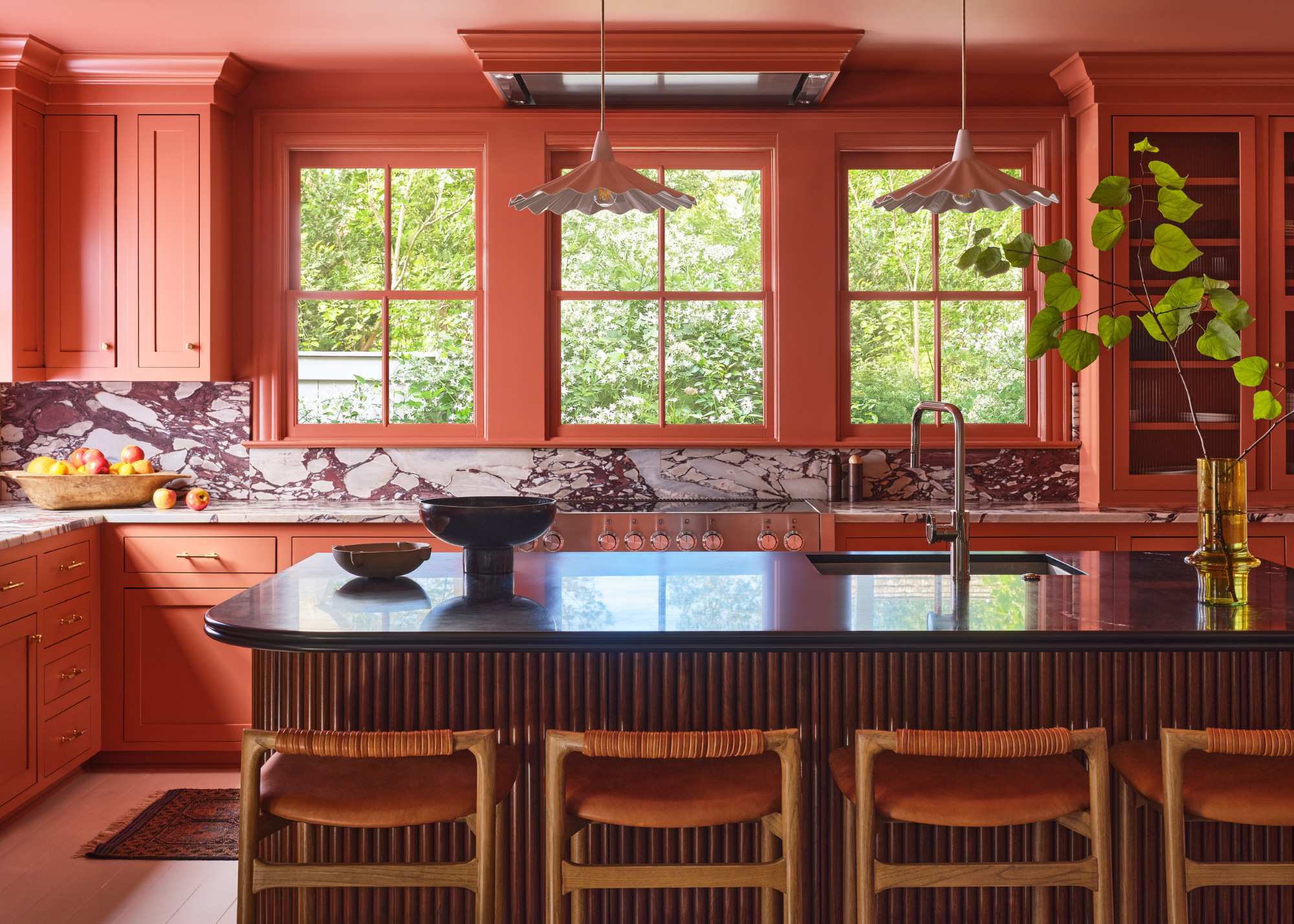 A bright terracotta kitchen with statement marble countertops and leather bar chairs