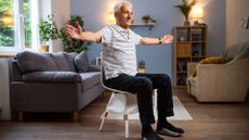 man sits on chair mid exercise with arms extended out 