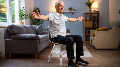 man sits on chair mid exercise with arms extended out 