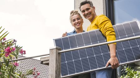 Man and woman standing on balcony holding solar panel