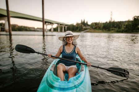 A Gen X woman of Pacific Islander descent smiling directly at the camera while kayaking along the Willamette River near Portland, Oregon.