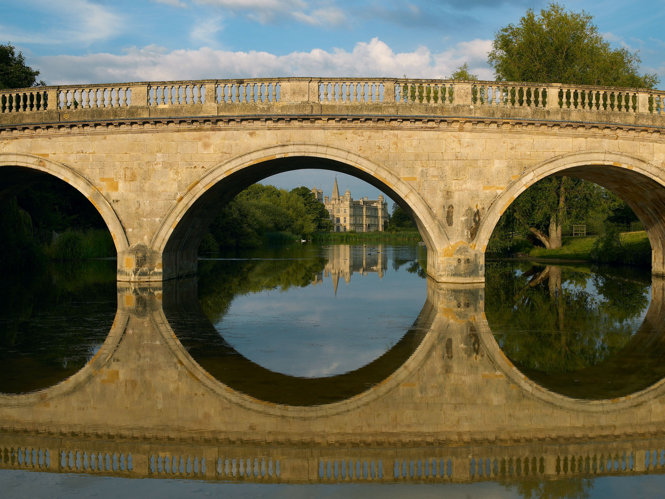 A view of Burghley House framed by the arches of the bridge designed by Capability Brown.