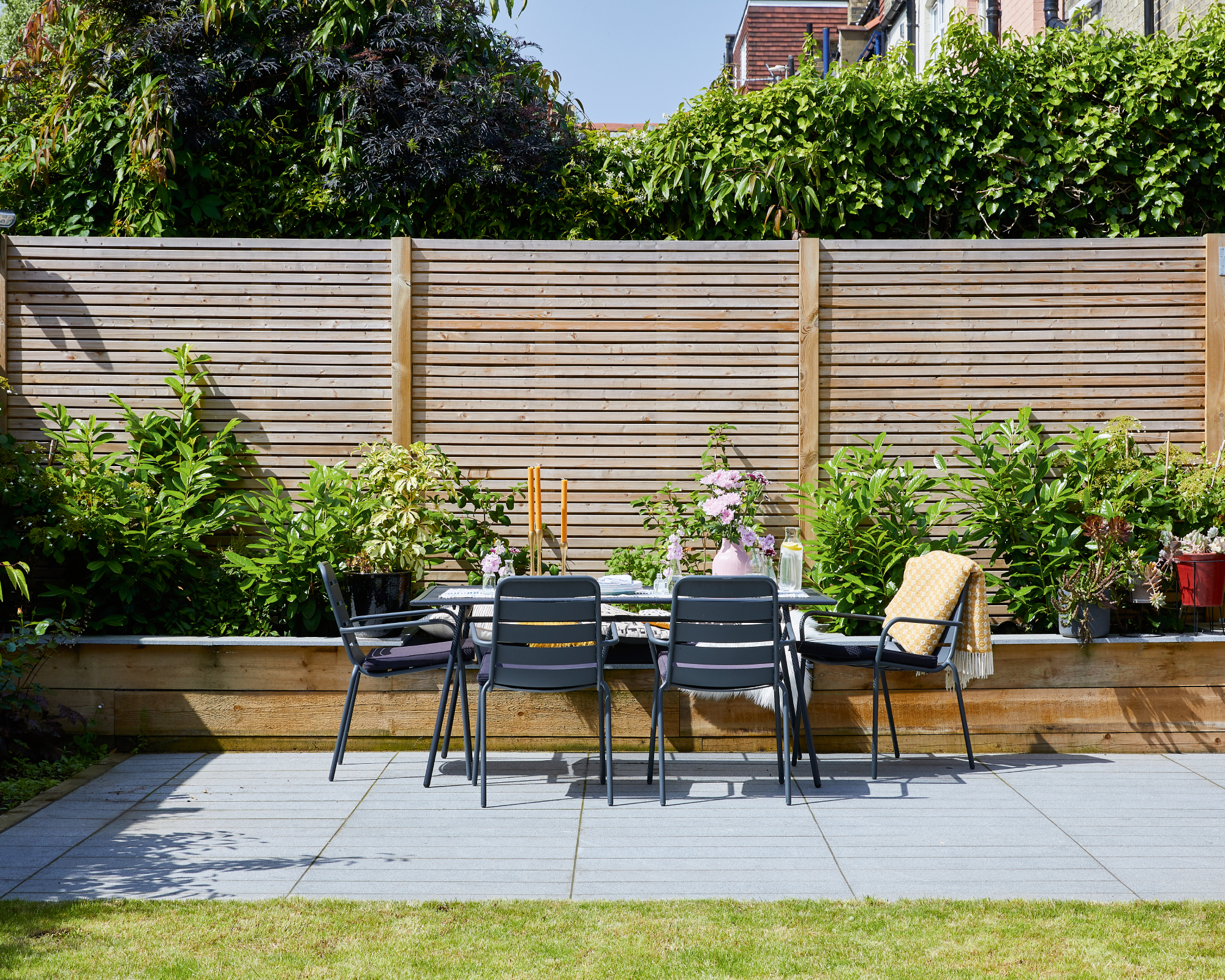 Table and chairs on the patio area in the garden beside raised flowerbed and wooden fence. The kitchen extension on Prue and Oner de Wynter's Edwardian terraced home in London.