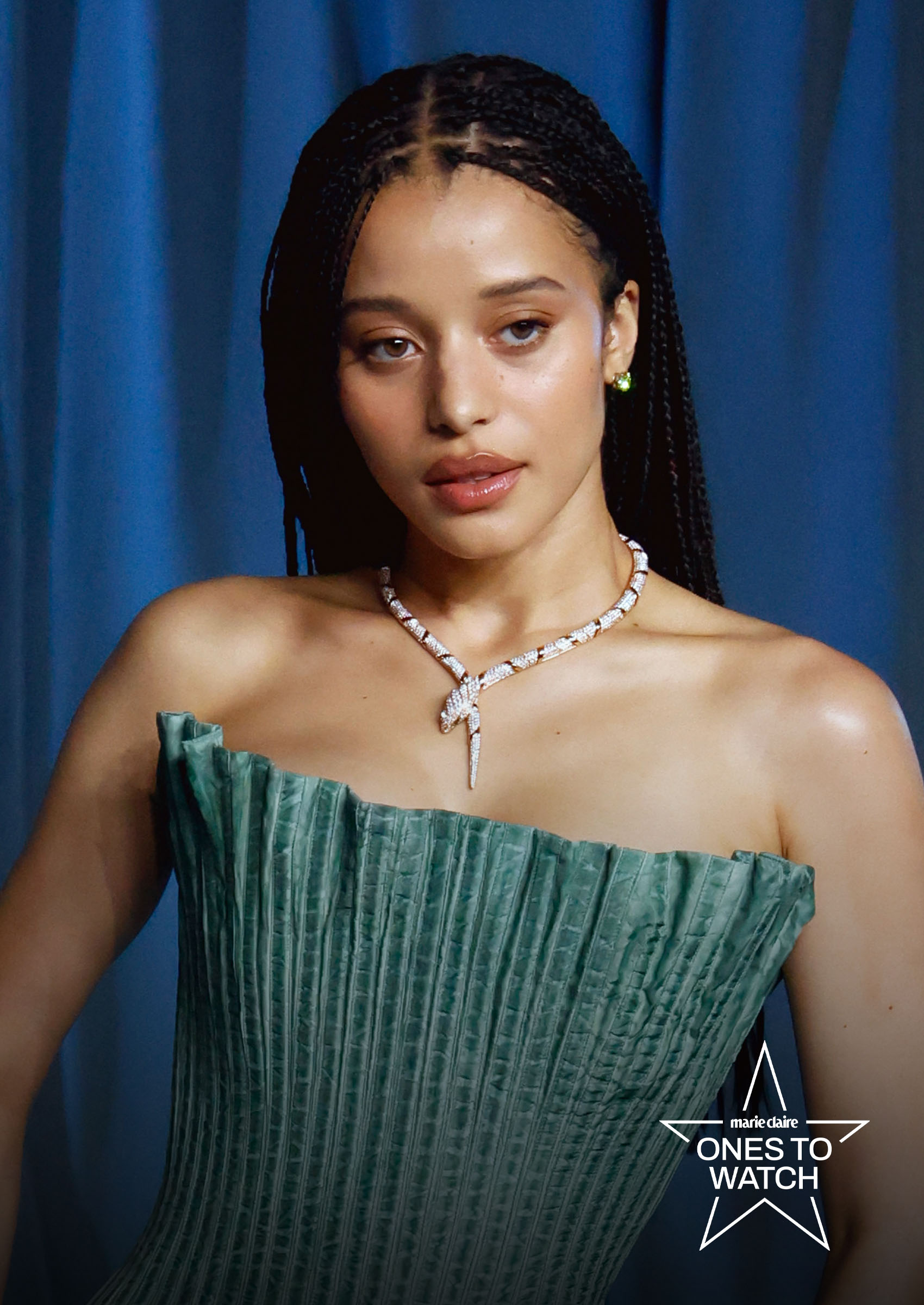 actress chase infiniti poses on a red carpet against a blue curtain wearing a snake necklace and green gown
