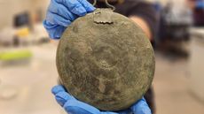 Gloved hands hold up the bronze folding mirror, showing its engraved exterior.
