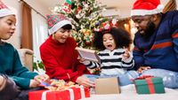 A family opening presents while wearing festive hats in front of a lit up tree.