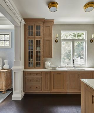 An oak kitchen with marble countertops and backsplash and the ceiling painted in a warm white hue