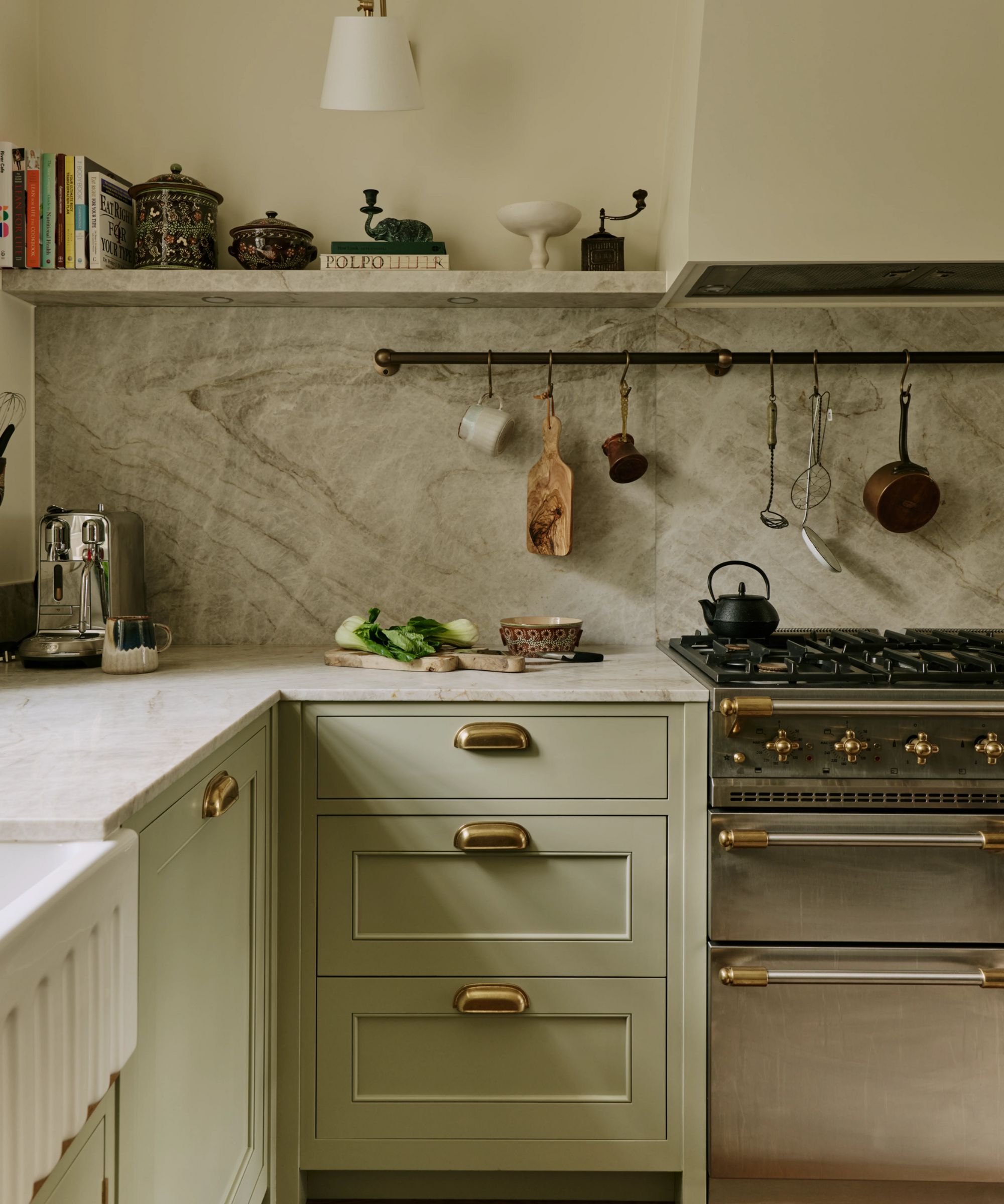a soft green kitchen with a stainless steel rangemaster cooker, custom hook and marble countertops and backsplash with a matching open shelf