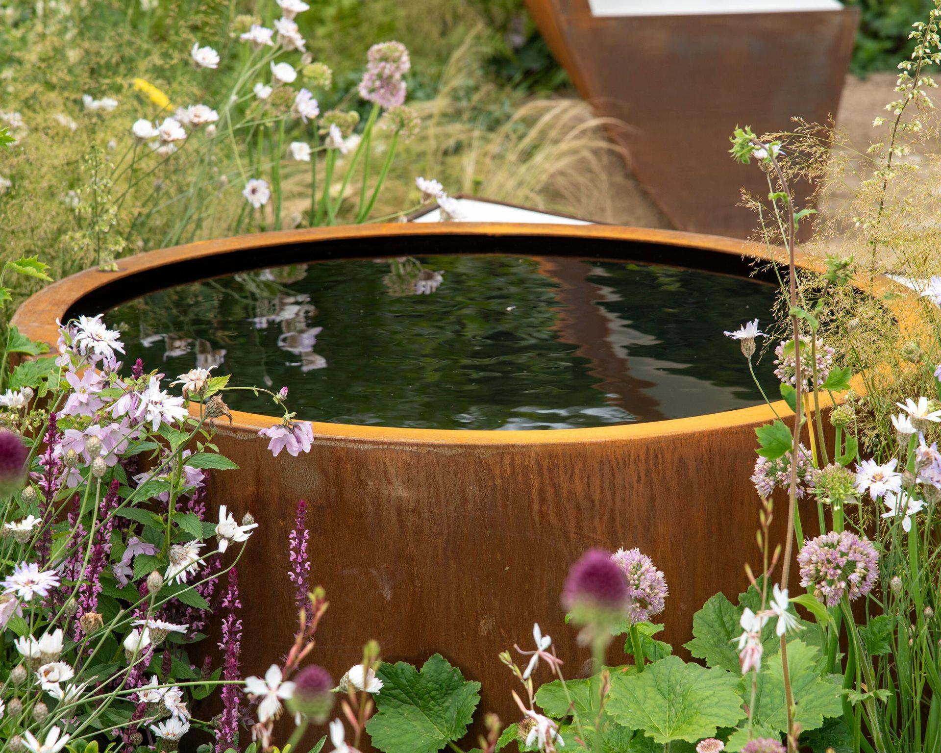 corten steel water feature surrounded by summer flowers and ornamental grass
