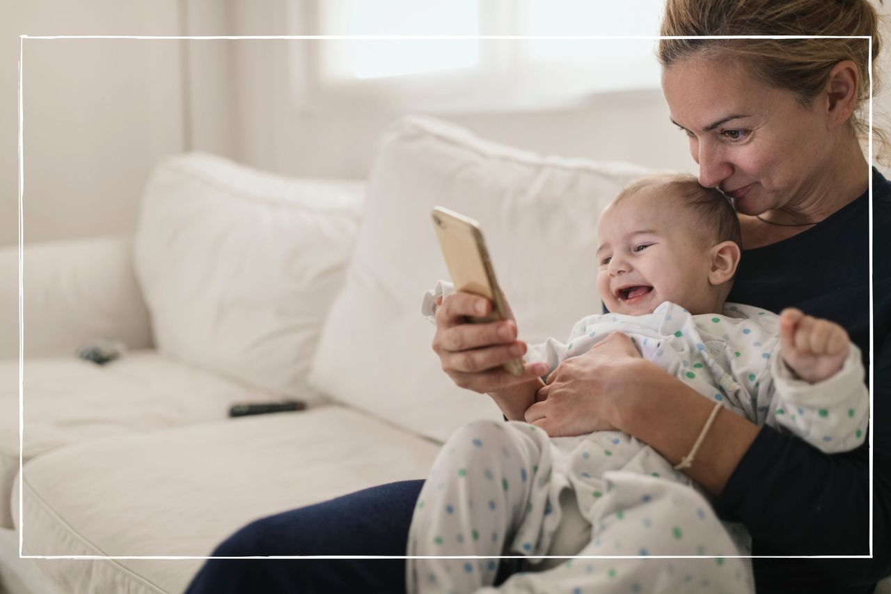 Smiling mother and baby sat on the sofa looking at a mobile phone