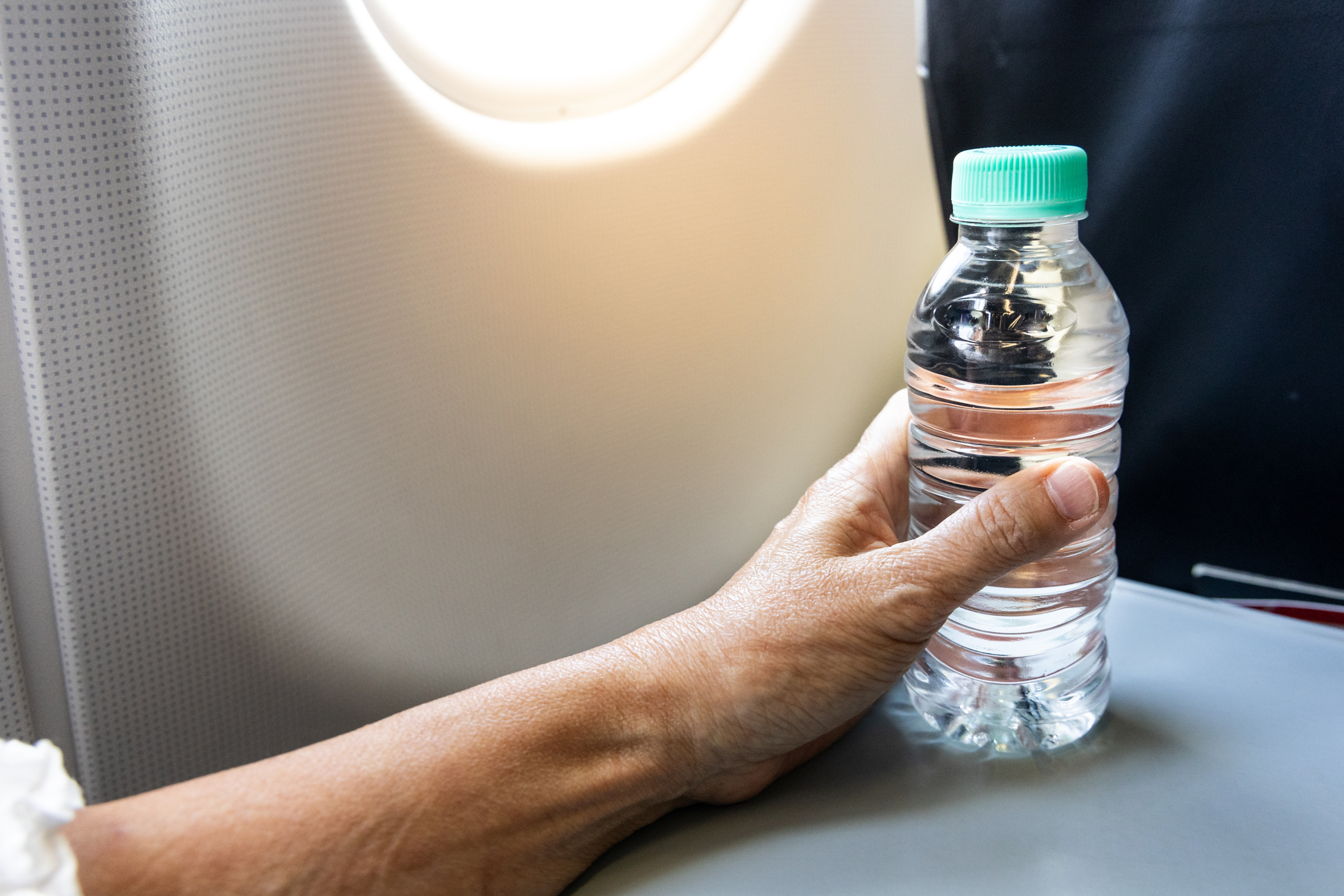 A hand holding a bottle of water on an airplane tray table