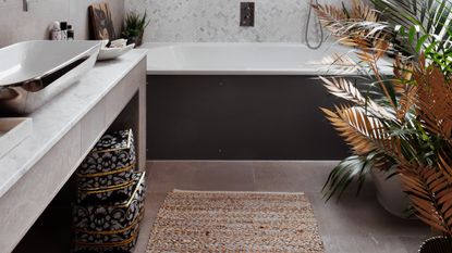 Dark bathtub in white bathroom with storage basket and bath mat