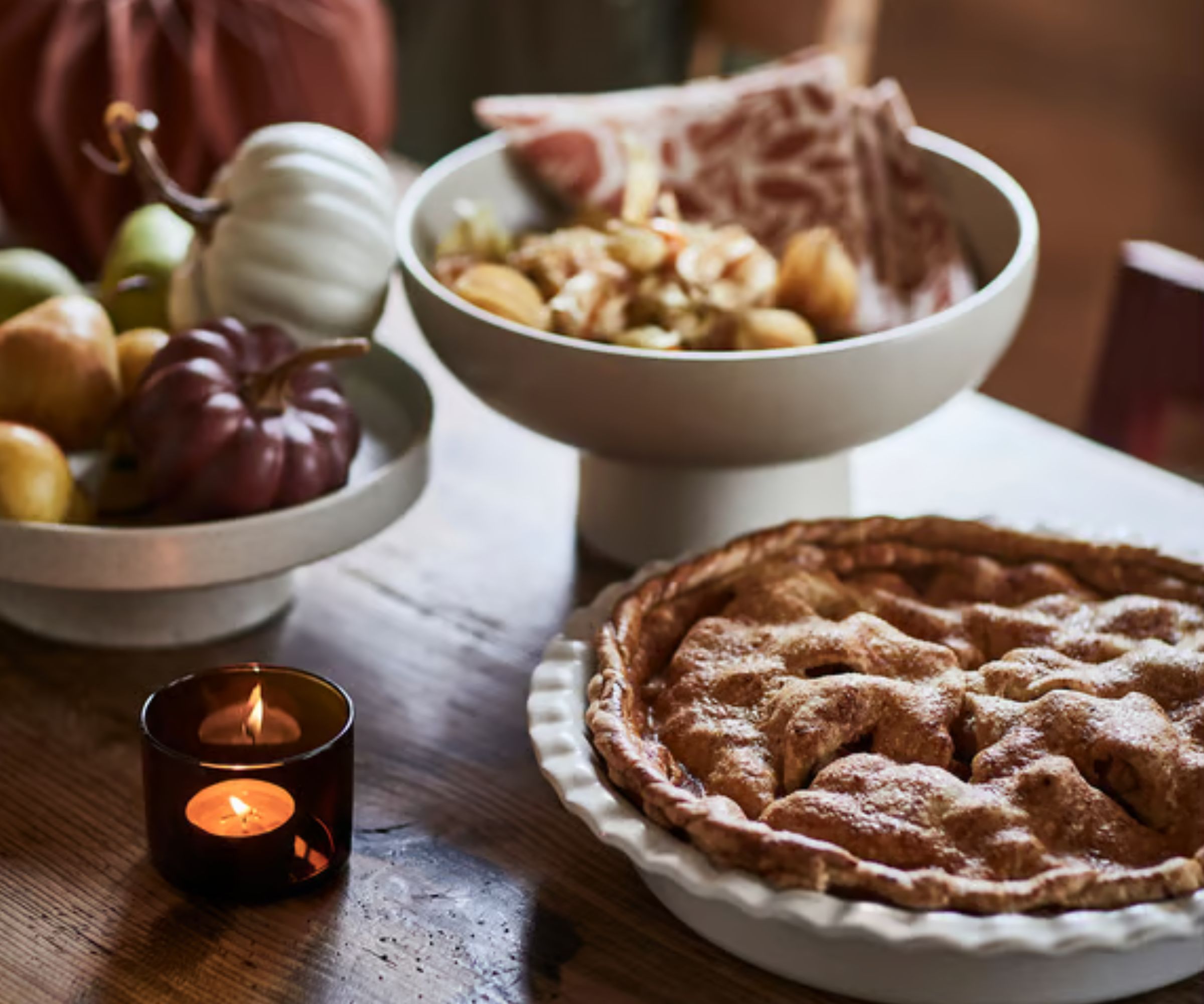 Table with ceramic bowl filled with dried flowers, pumpkin decorations, tealight and pie dish