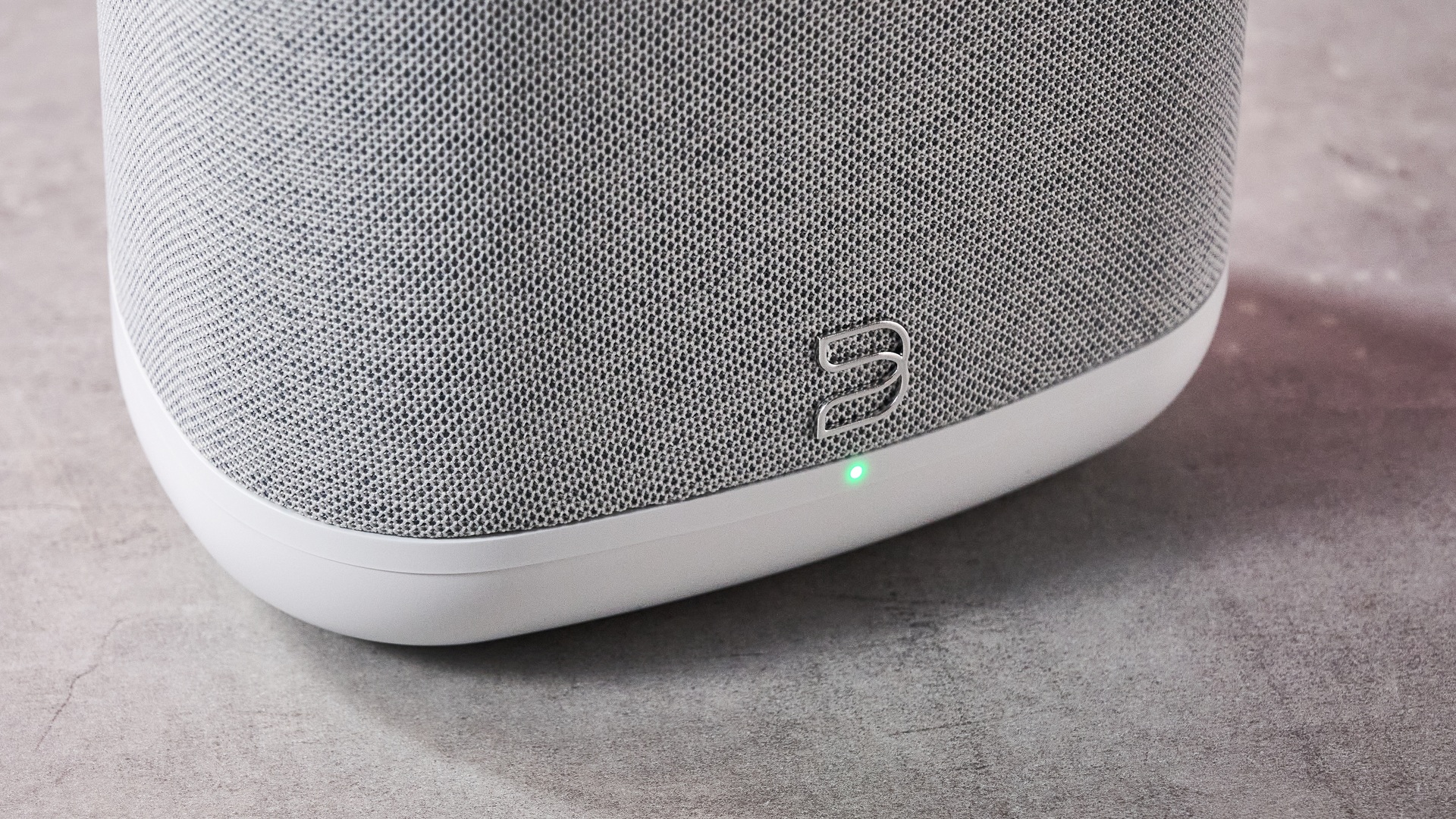 A closeup of the Bluesound logo on the front of the Bluesound Pulse Flex; its LED indicator is lit up in green.