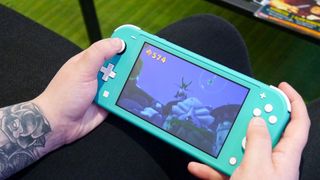 En person sitter och spelar på en blå Nintendo Switch Lite.