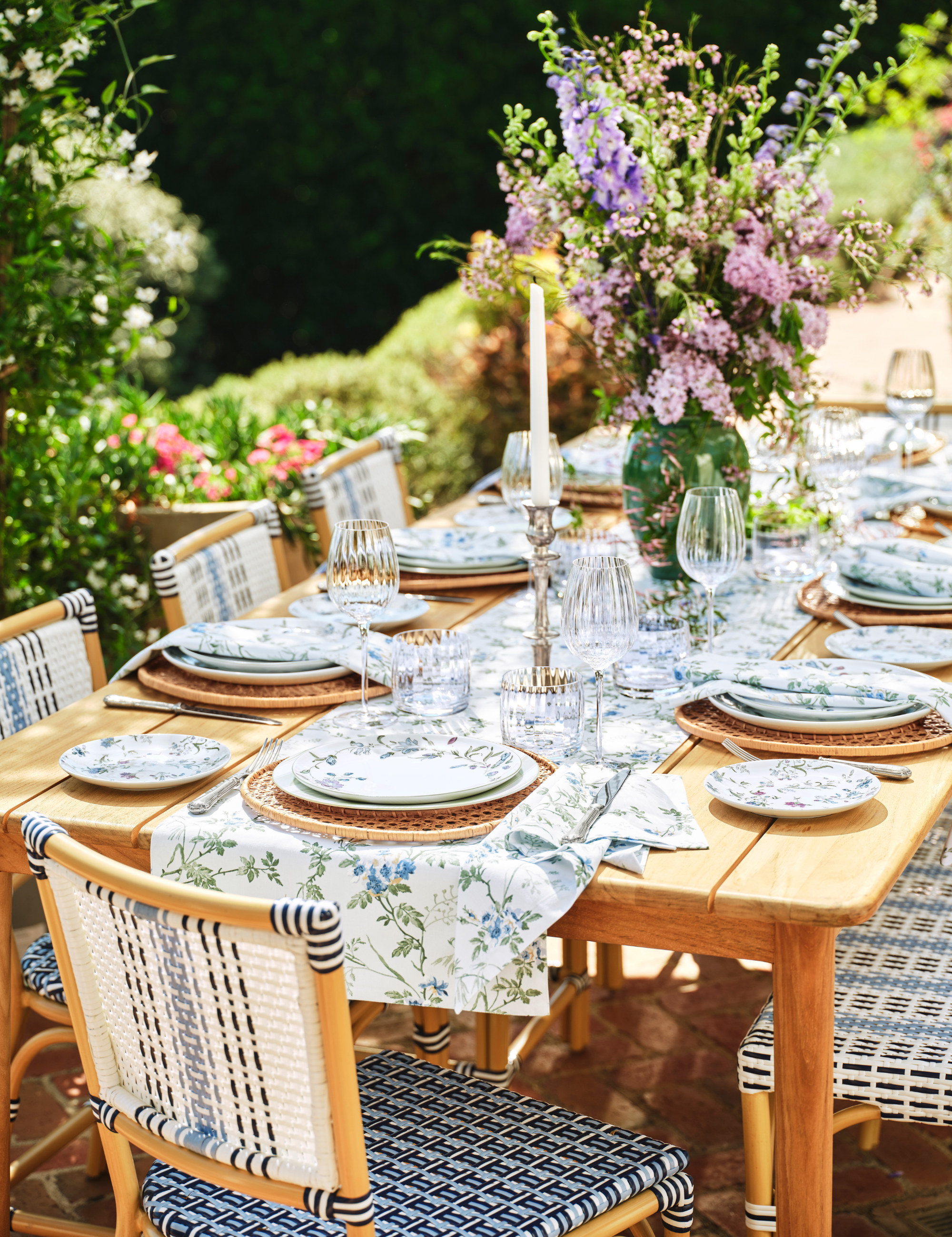 Charming alfresco tablescape featuring woven wicker outdoor dining chairs, floral table linens, and patterned plates.