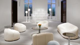 White room with white chairs, a glass coffee table and floor lamps designed by Pierre Paulin displayed at Sotheby's