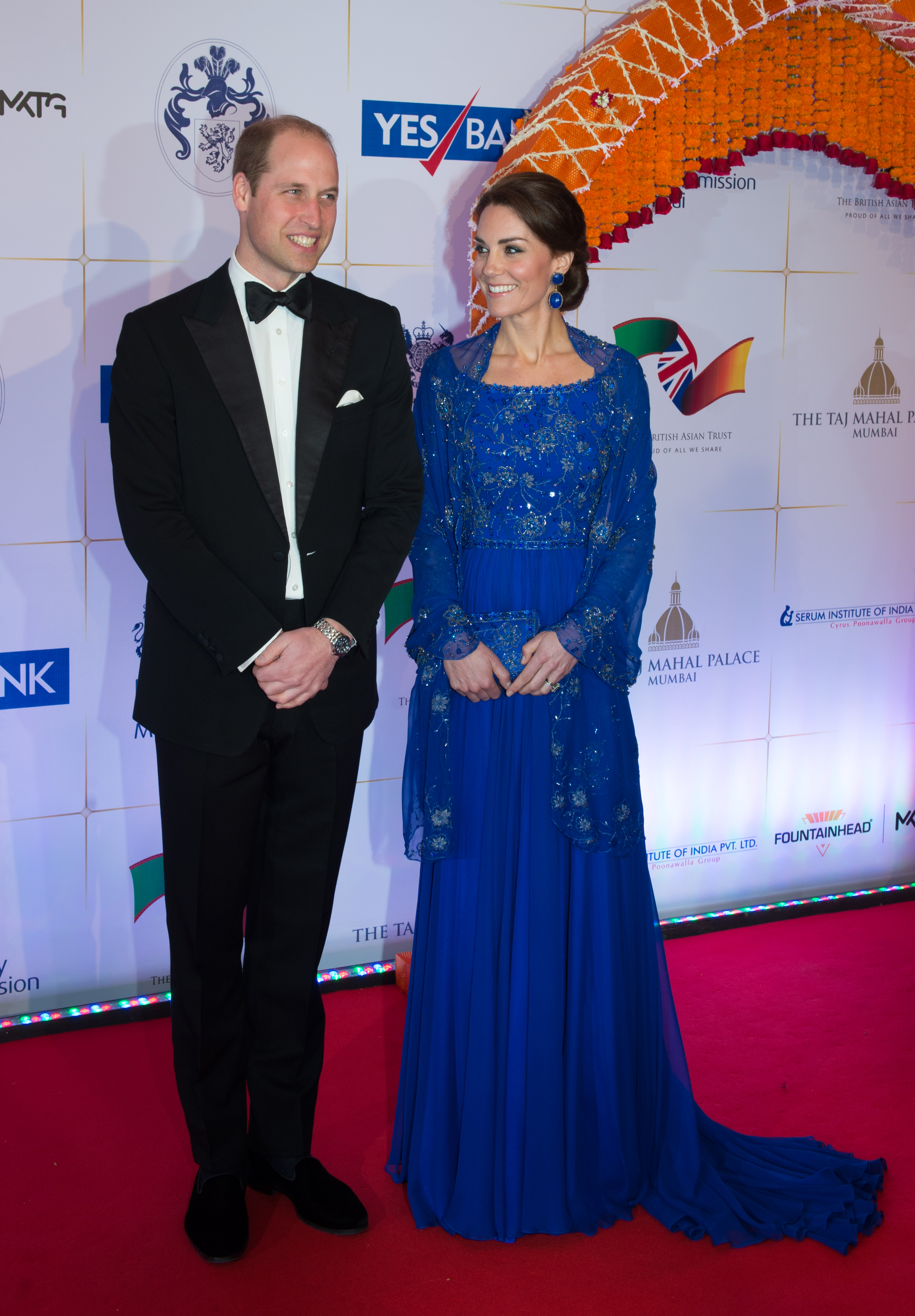 Prince William wearing a tux, Princess Kate wearing a blue beaded gown on a red carpet