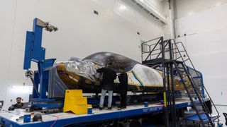 a white and black space plane sits inside a large white-walled room