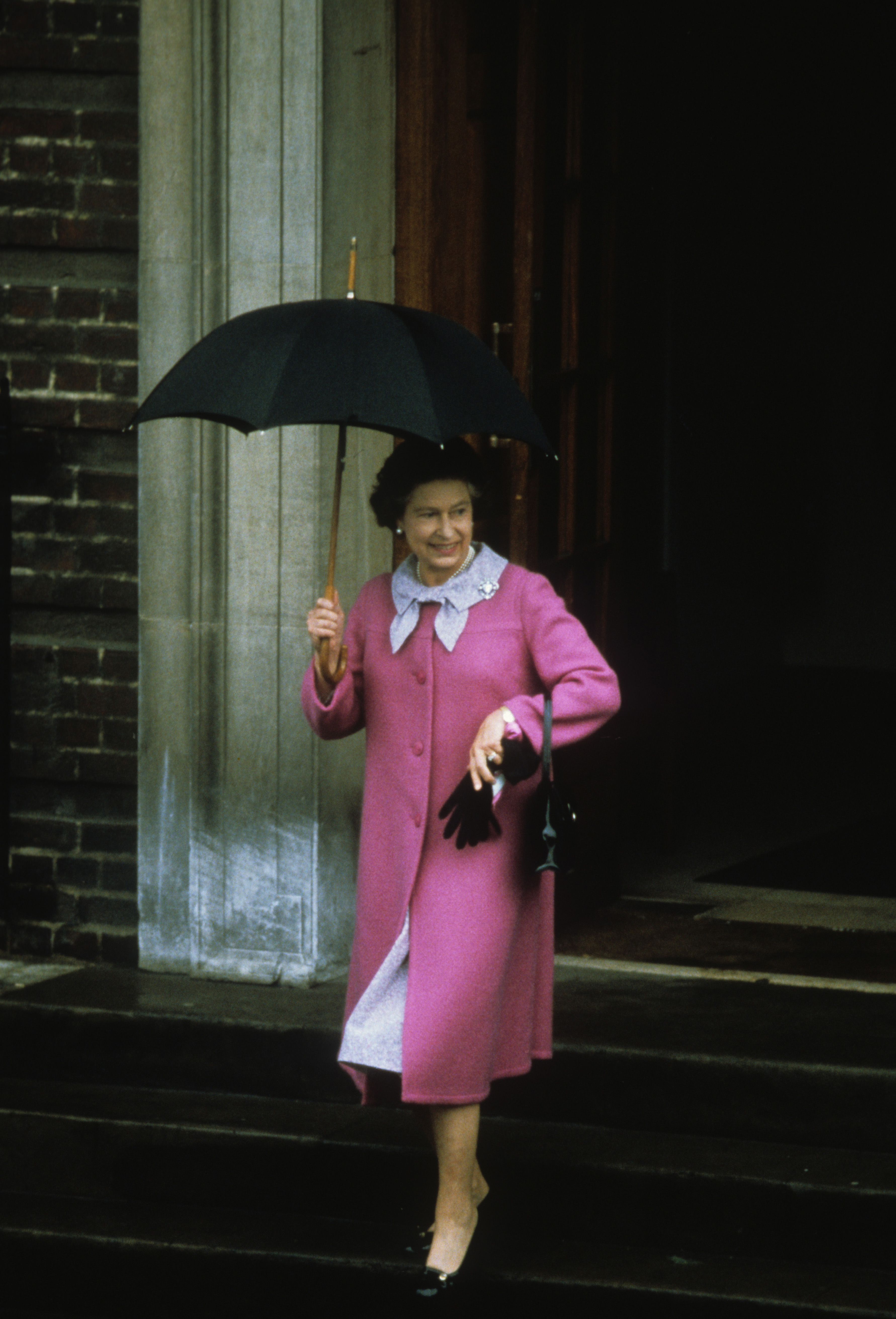 Queen Elizabeth II wears a pink coat and holds a black umbrella leaving the Lindo Wing after Prince William's birth, and the Royal Family poses for photos at William's christening