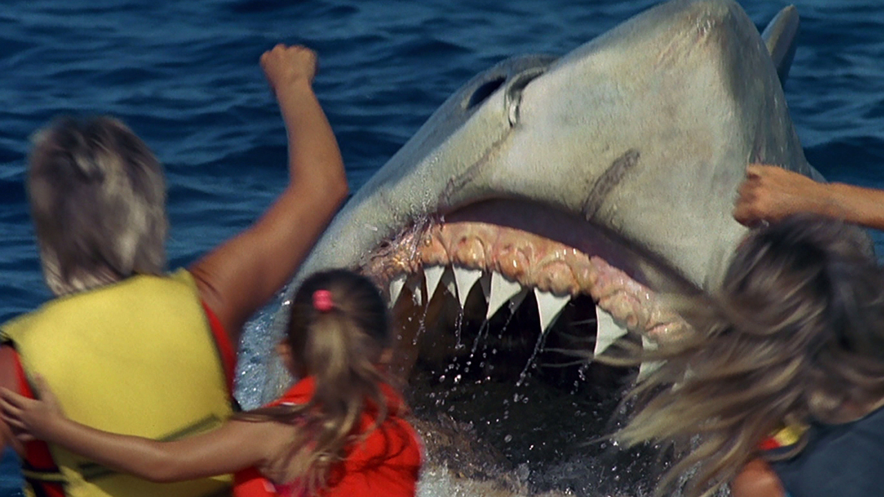 Standbild aus dem Film Jaws: The Revenge.  hier sehen wir eine nahaufnahme des mauls eines riesigen weißen hais, der auf eine junge familie zuspringt.