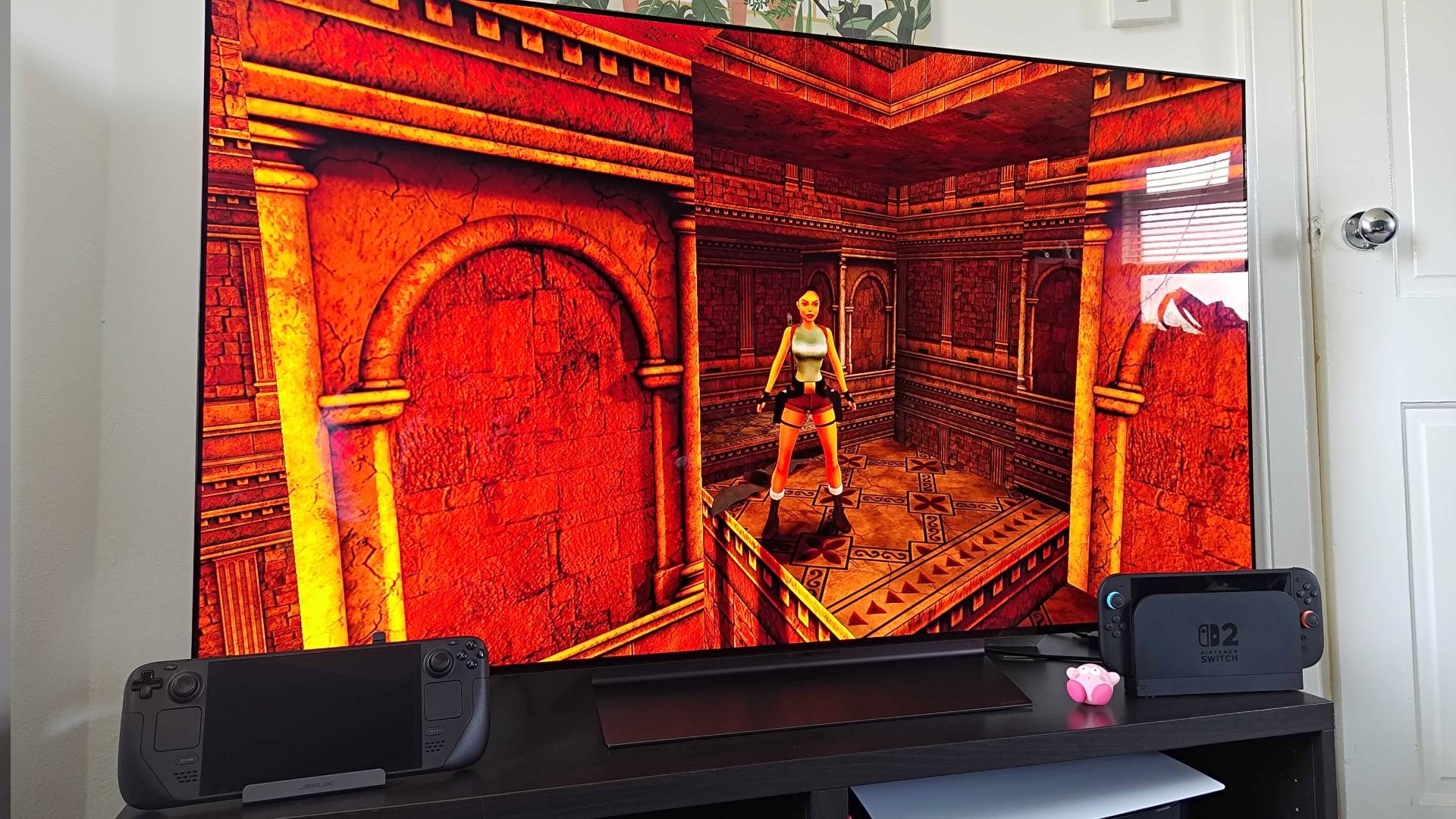 Steam Deck OLED connected to LG OLED C4 TV via Jsaux dock on bench with Switch 2 on right and Tomb Raider gameplay on screen.
