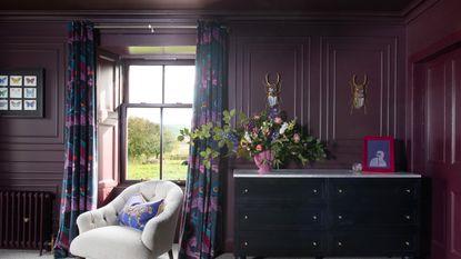 A dressing room colour drenched in an aubergine purple paint with dark floral curtains