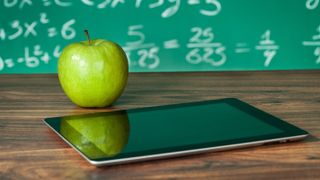 Apple iPad on desk with apple and blackboard behind showing math equations