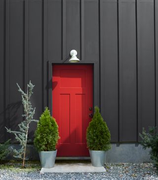 The exterior of a house with a red door and walls painted in a dark gray-black shade