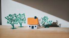 Tiny house with an orange roof in sunlight, casting shadow, surrounded by toy trees.