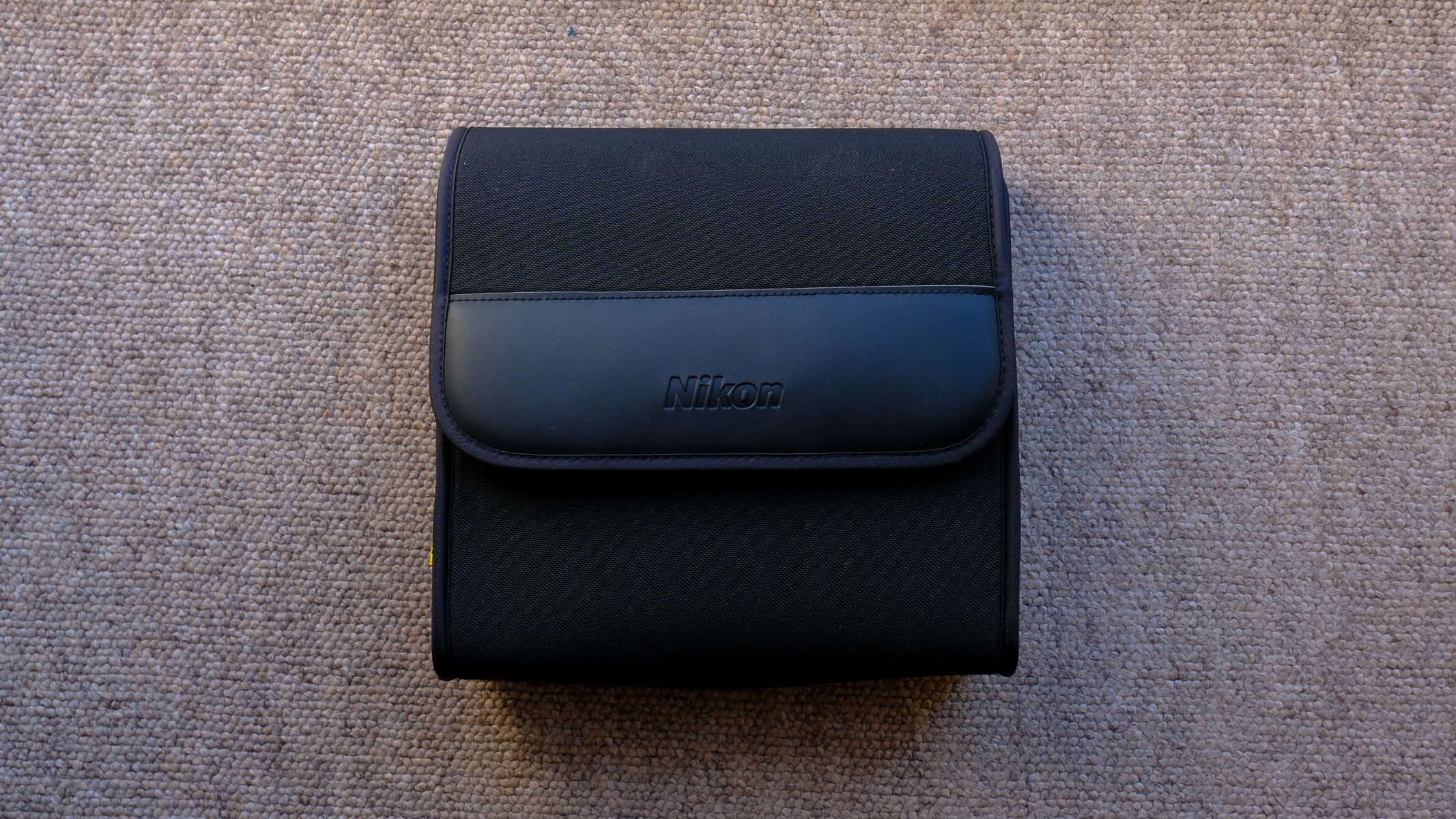 The closed protective case for the Nikon Action 7x50 binoculars on a brown carpet.
