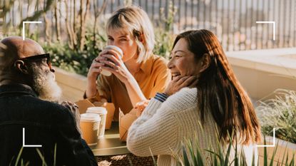 Three friends laughing and talking together drinking coffee from cups, representing social interaction to learn how to stop feeling sad