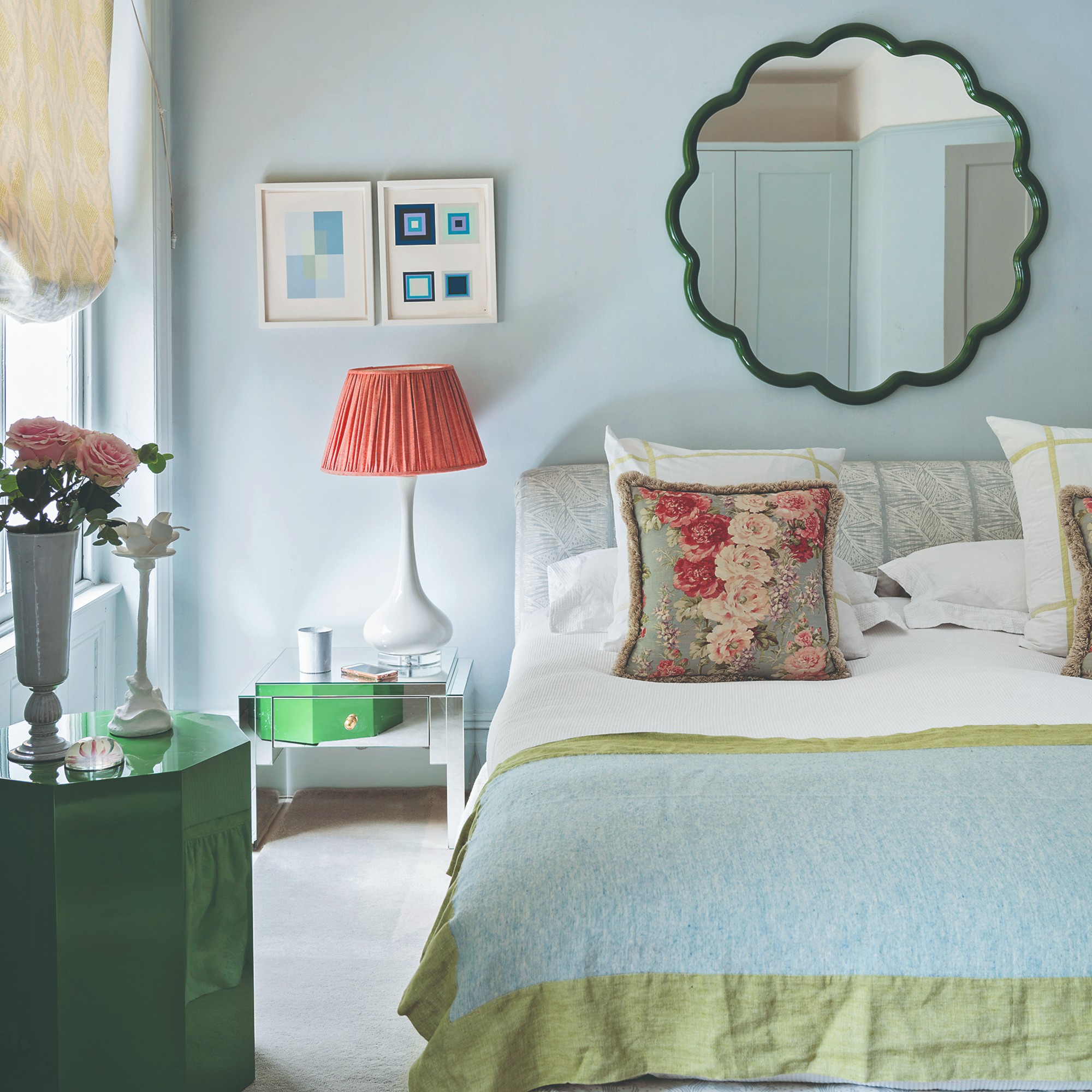 A light blue-painted bedroom with a bright green side table and scalloped mirror hung above the bed